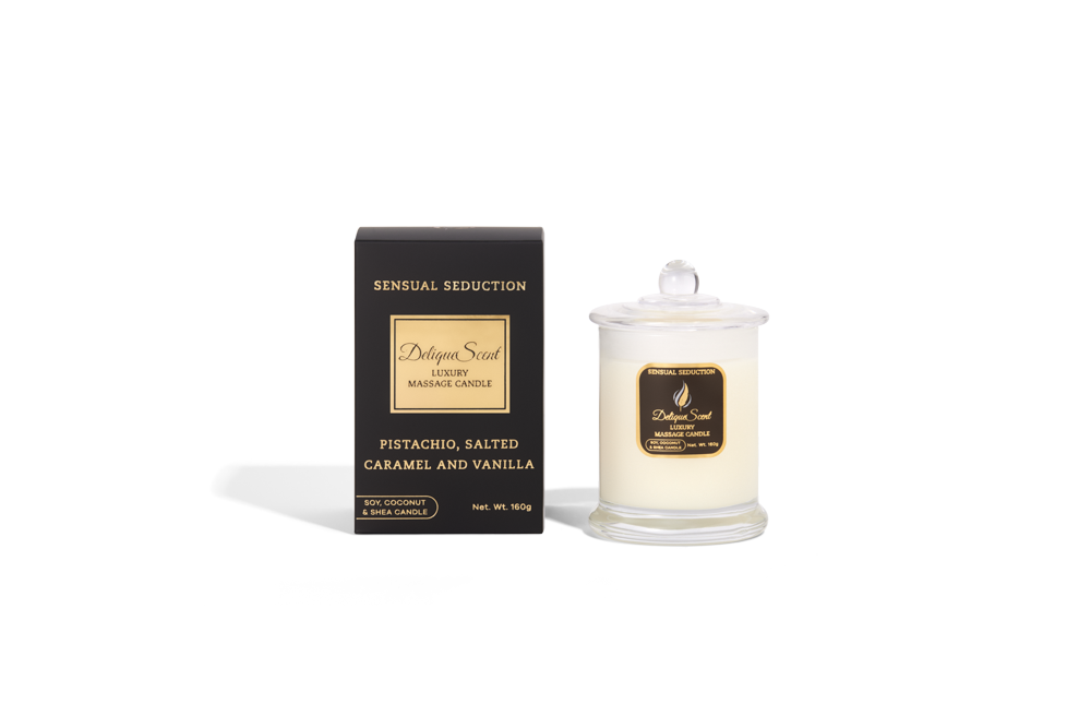 Body Safe, Organic Massage Candle in Sensual Seduction Scent, which is Pistachio, Salted Caramel and Vanilla fragrance Gold Highlights on a black box next to the glass massage candle.